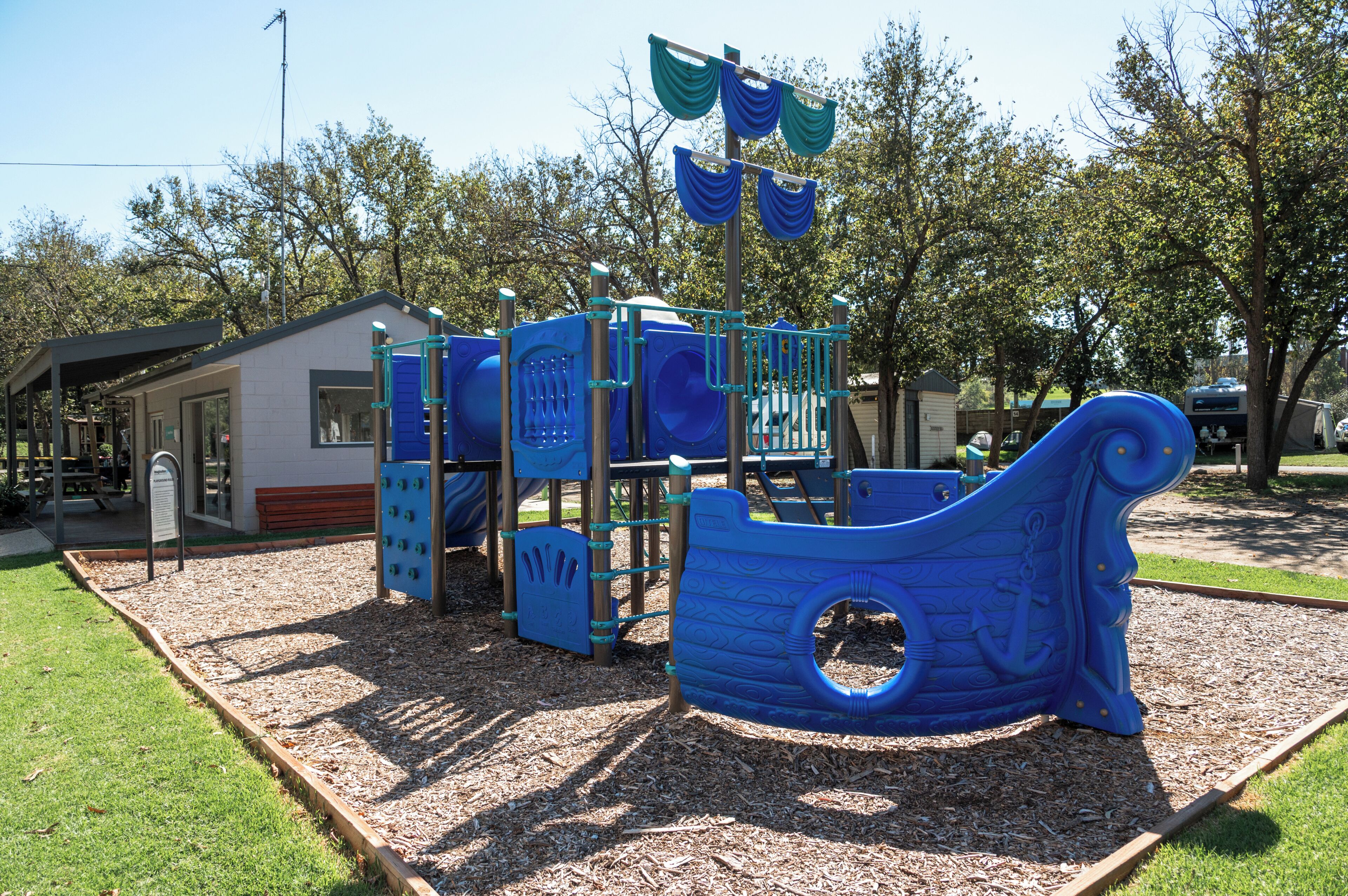 A playground with a ship-themed play structure, surrounded by trees and a picnic area.