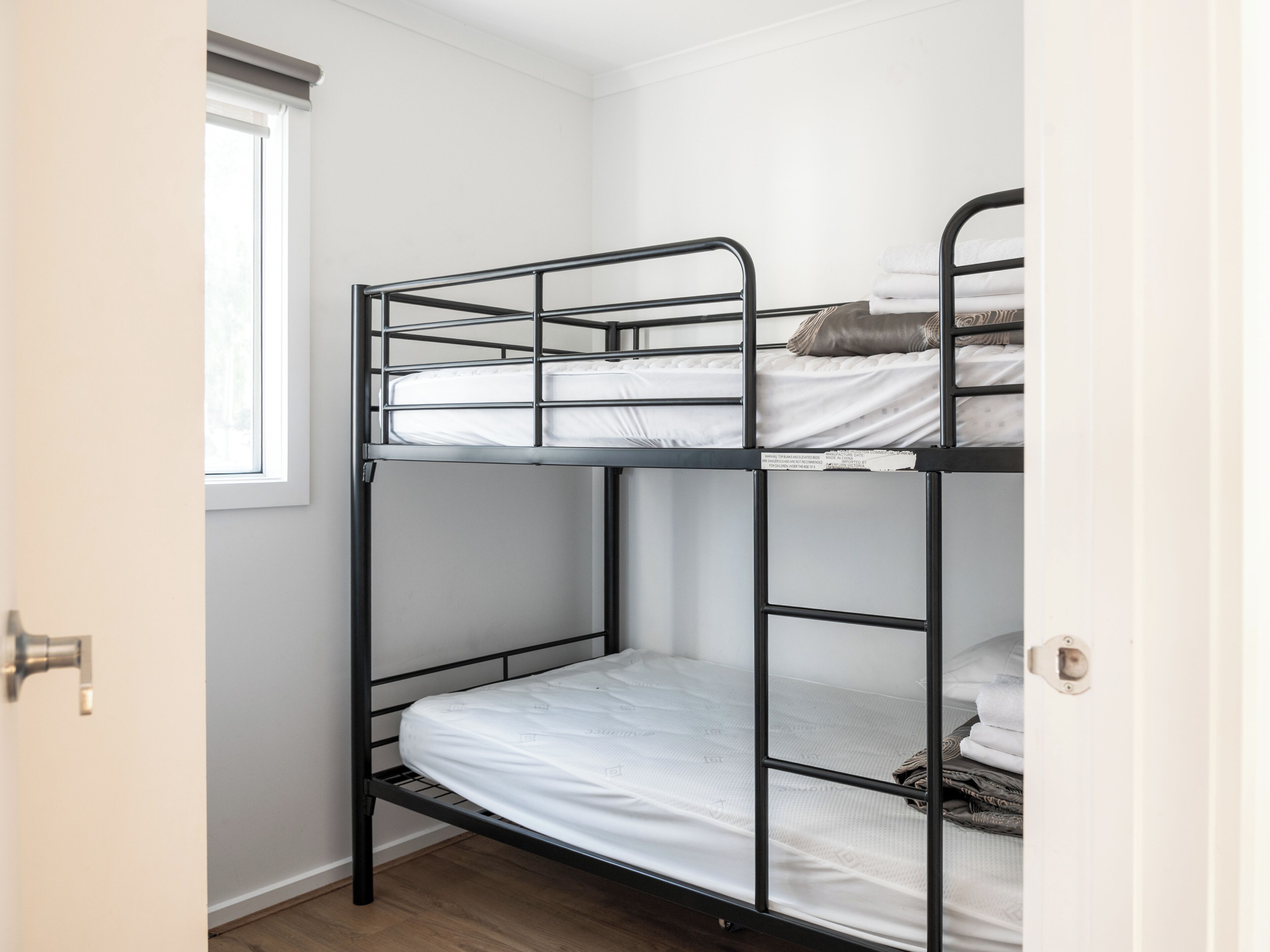 A bunk bed with a window, a door, and a wooden floor.