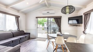 A modern living room with a sofa, dining table, chairs, a TV, and a balcony. - Geelong Holiday Park (Belmont)