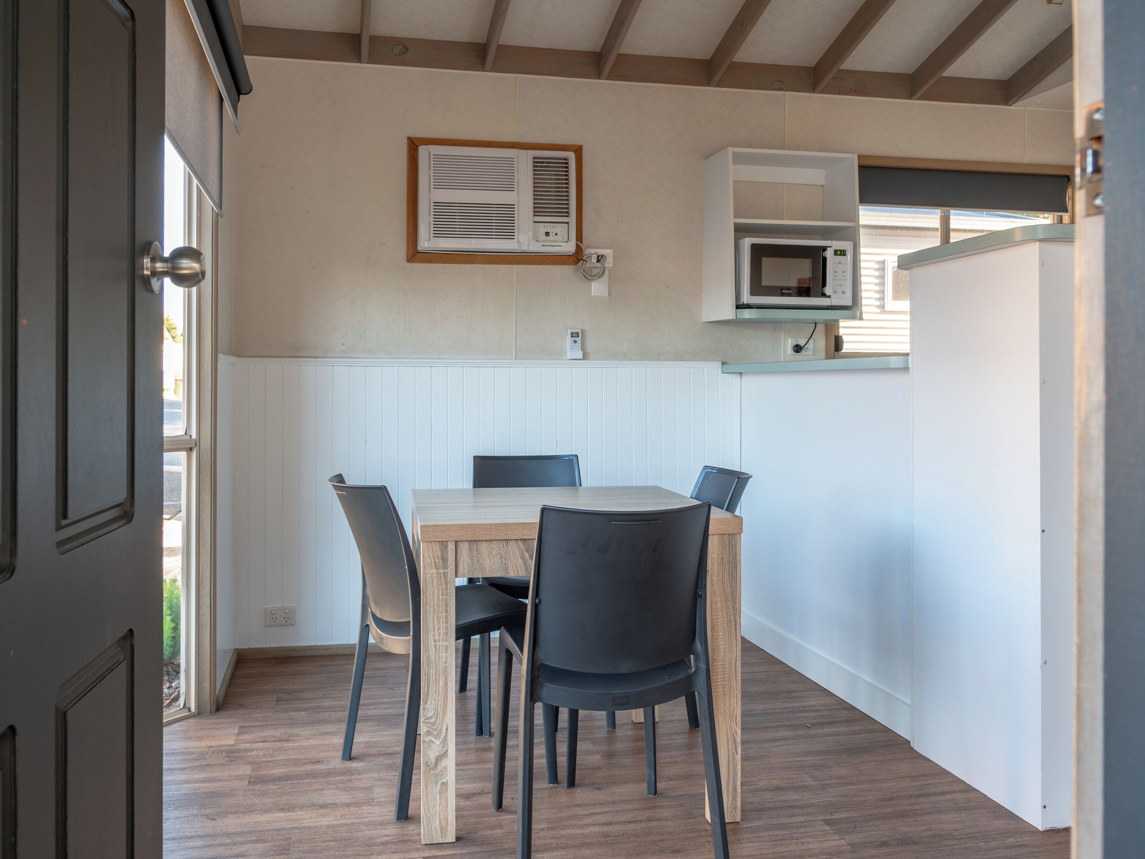 A compact kitchen with a dining table, chairs, a microwave, and a wall-mounted air conditioning unit.