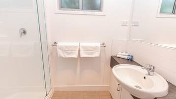 A modern bathroom with a glass shower enclosure, a white sink, and a window above the mirror.