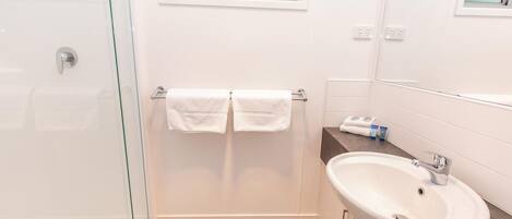 Un baño moderno con cabina de ducha de vidrio, un lavabo blanco y una ventana sobre el espejo.