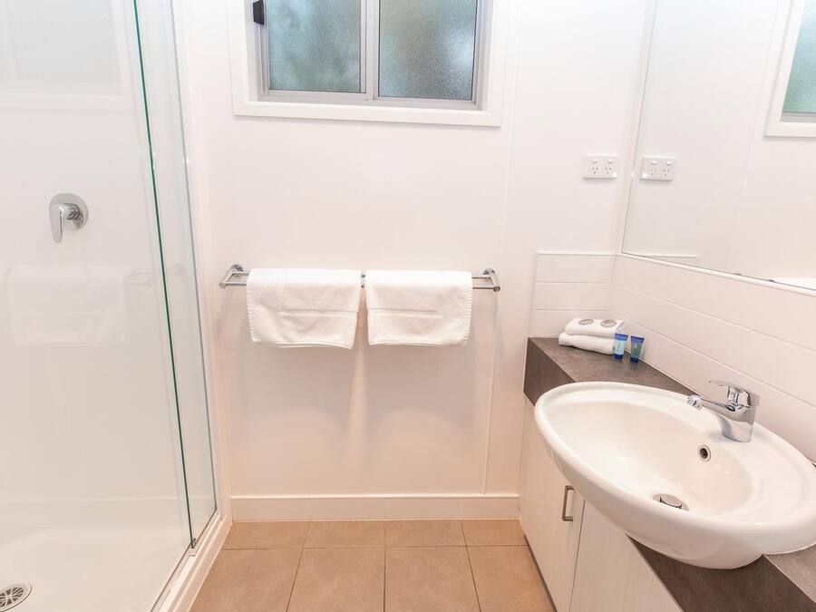 A modern bathroom with a glass shower enclosure, a white sink, and a window above the mirror.