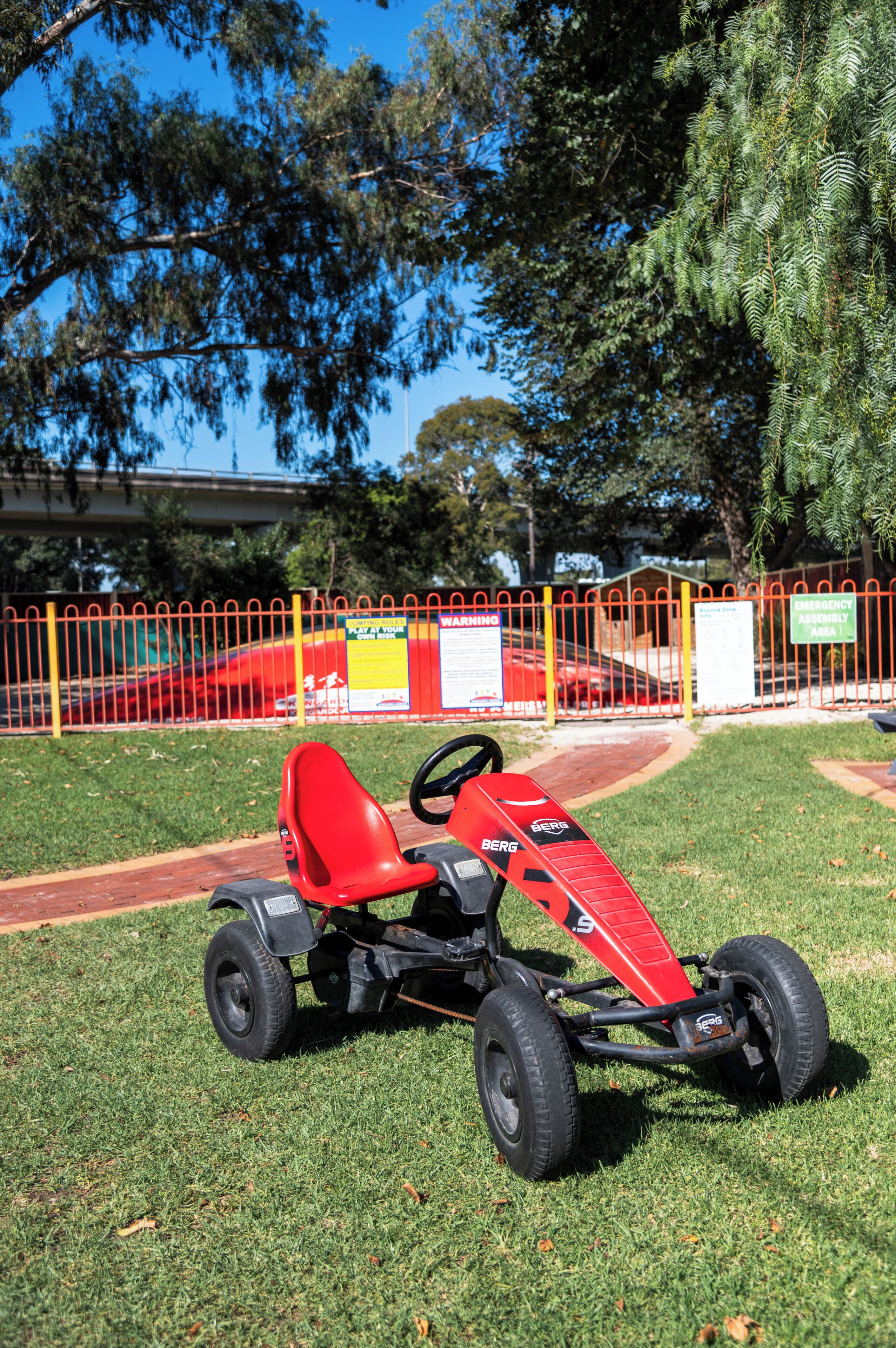 A red go-kart on grass with a fenced area in the background.