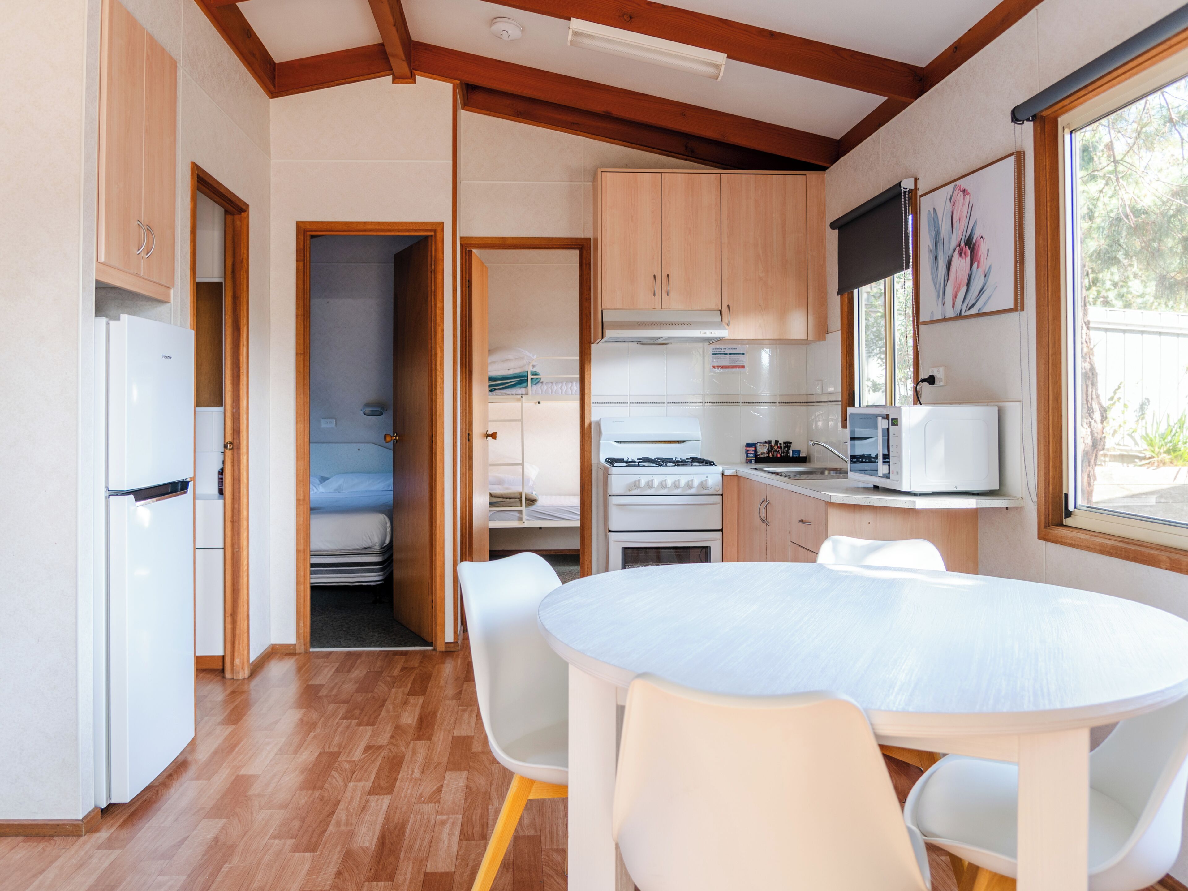A compact kitchen with wooden cabinets, a white refrigerator, a stove, and a microwave. There is a dining table with chairs.