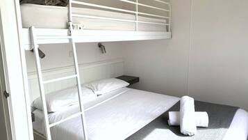 Habitación con literas, cabecera blanca, mesita de noche y una toalla enrollada en la litera inferior.