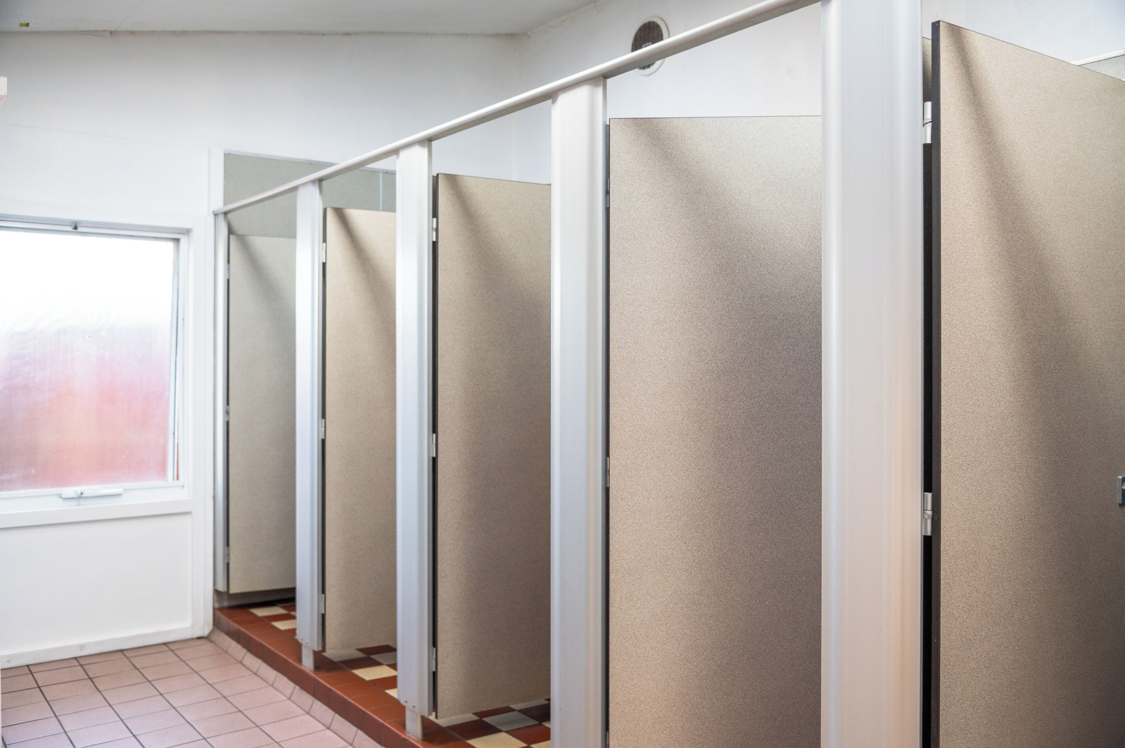 Fila de cabinas de baño individuales con una ventana a la izquierda.