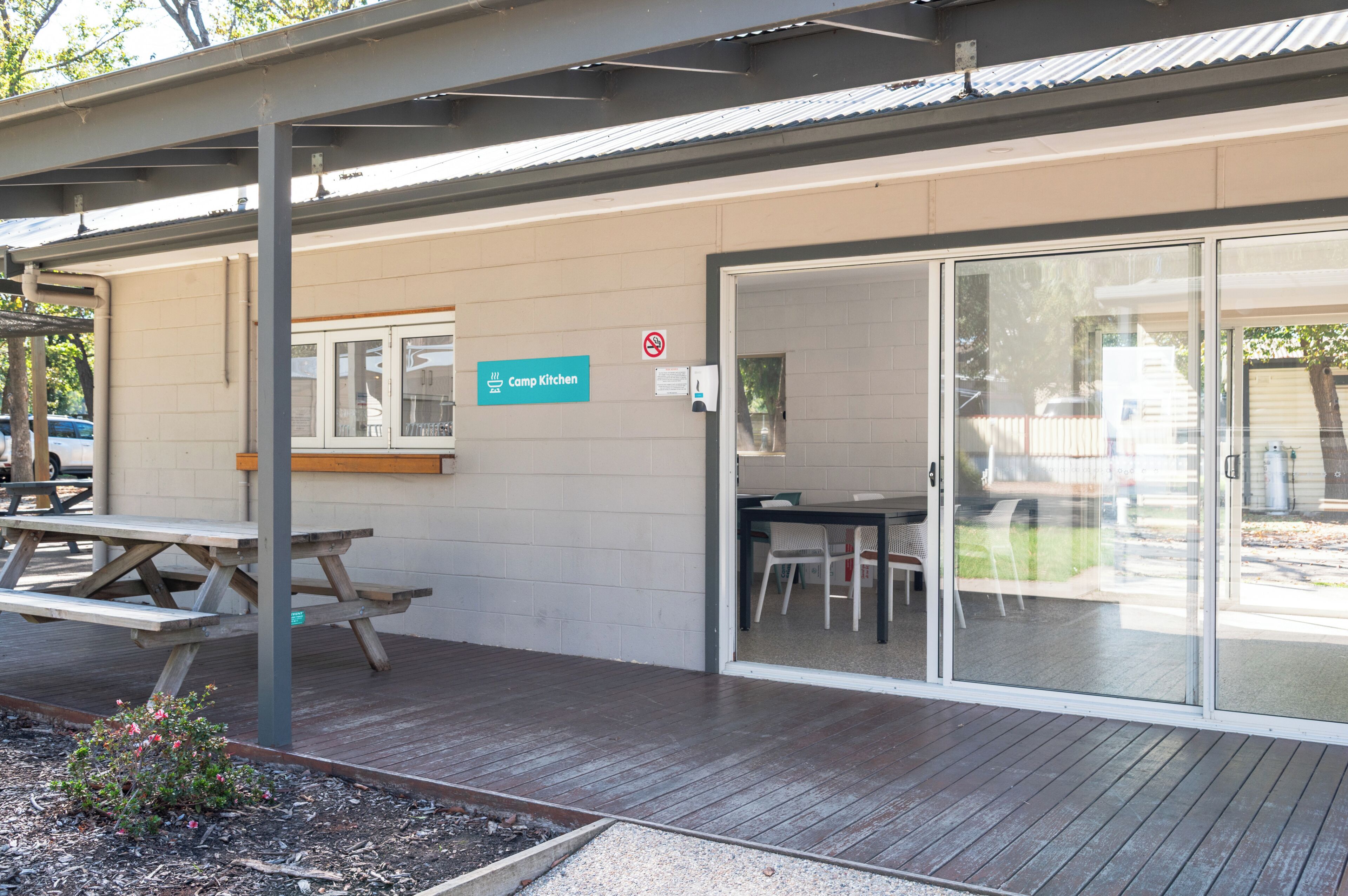 A building with a sign reading 'Camp Kitchen,' a picnic table, and a glass door entrance.
