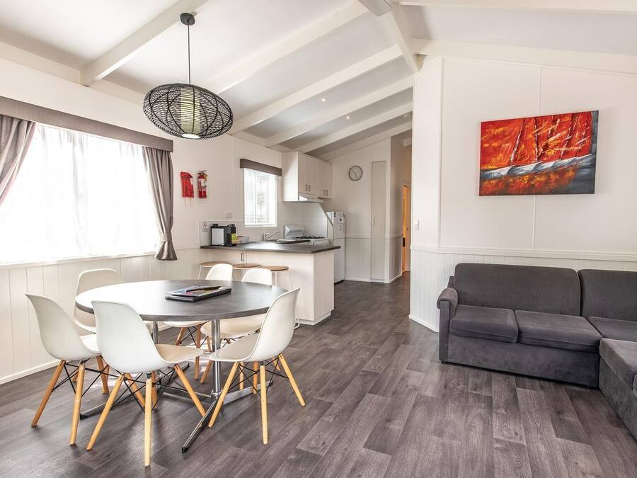 A modern living room with a grey sofa, a dining table with white chairs, and a kitchen area in the background.
