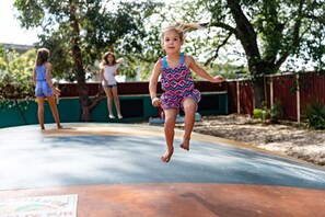 A child jumping on a trampoline in an outdoor setting with a wooden fence and trees in the background. - Geelong Holiday Park (Belmont)