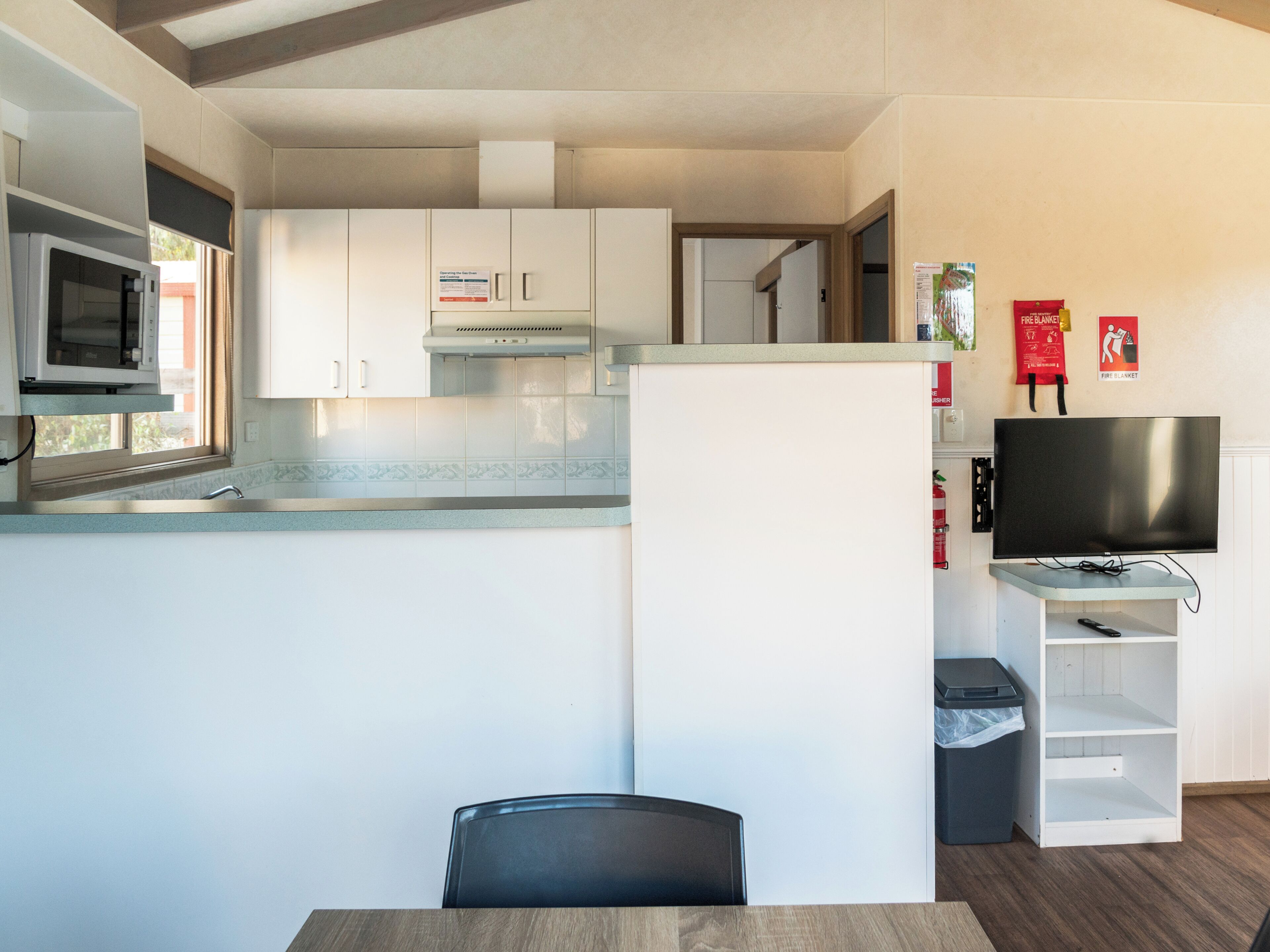 A compact kitchen with white cabinets, a microwave, and a stove. There's a TV on a stand and a trash bin.