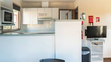 A compact kitchen with white cabinets, a microwave, and a stove. There's a TV on a stand and a trash bin.