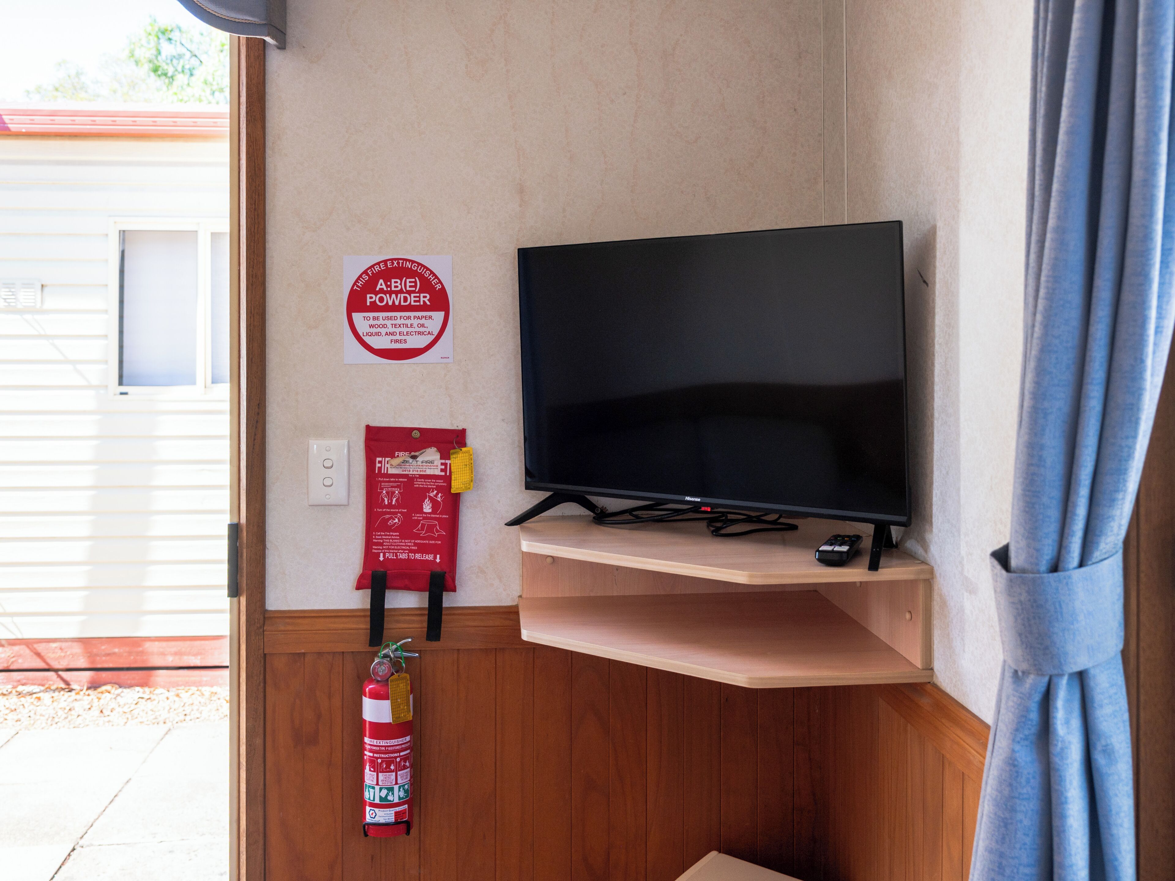 A room with a television on a stand, a fire extinguisher, and a fire safety sign on the wall.