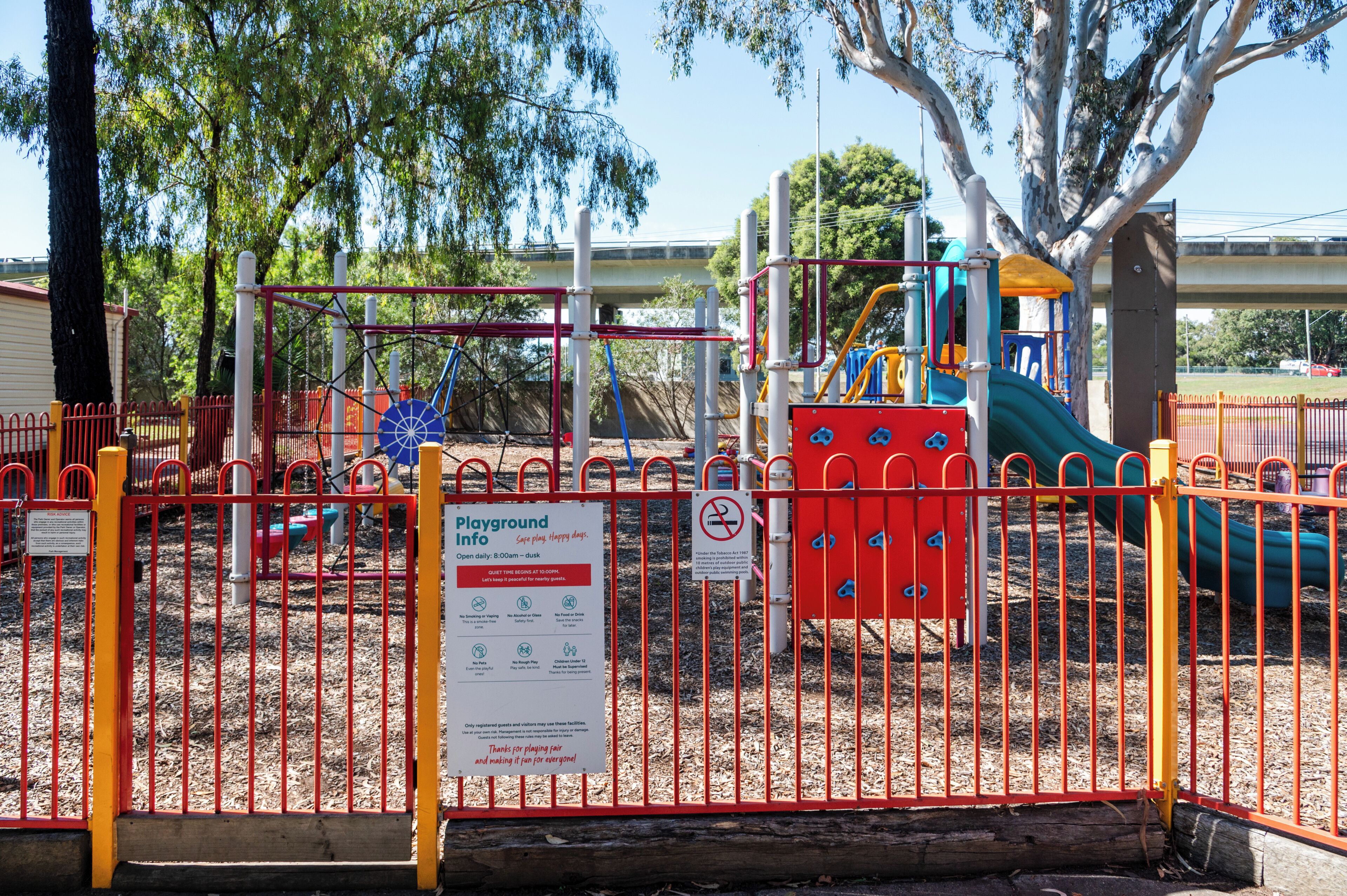 A playground enclosed by a red fence with various play structures, including slides and climbing areas.