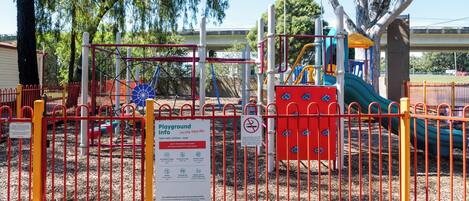 A playground enclosed by a red fence with various play structures, including slides and climbing areas.