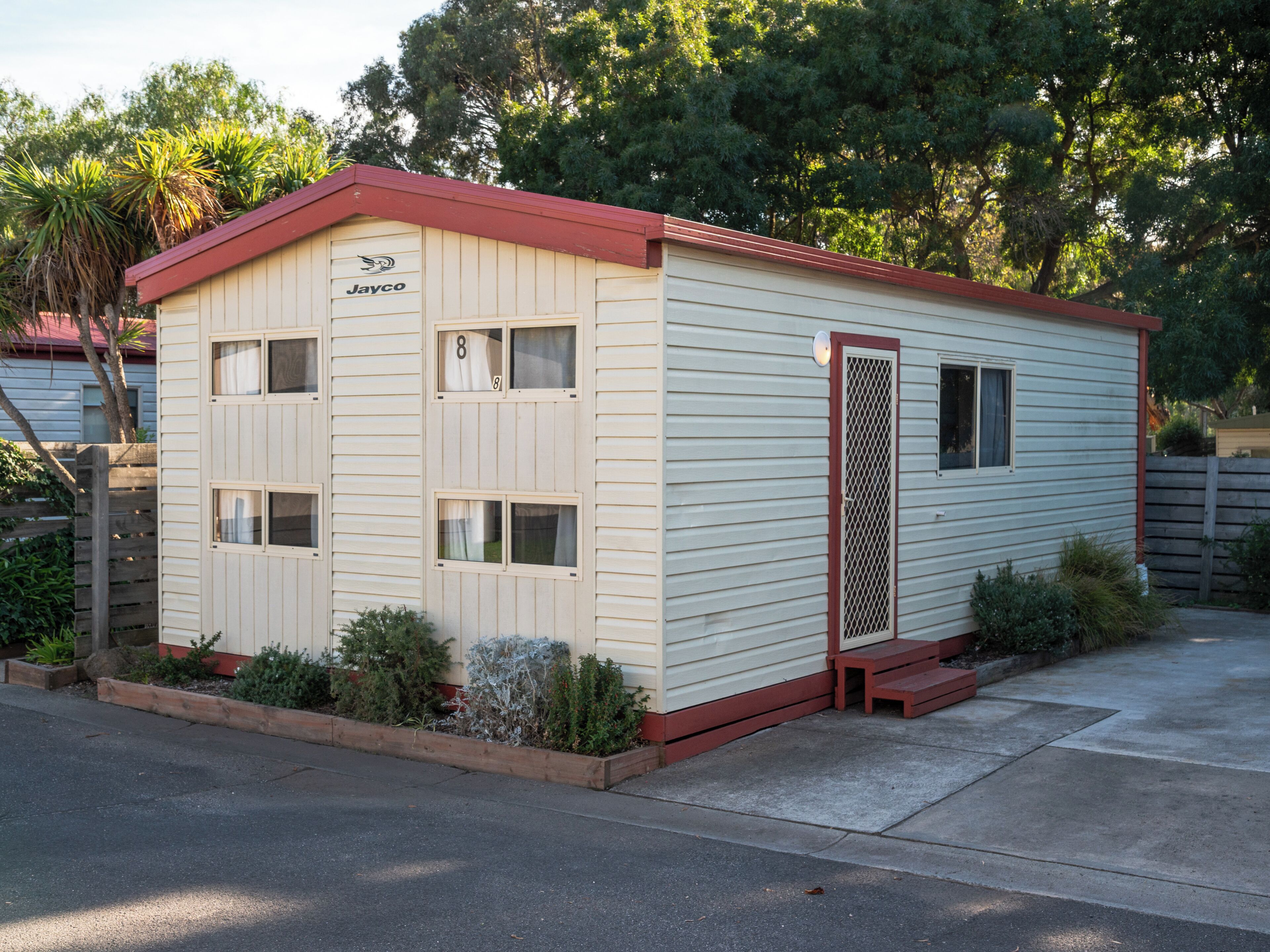 Un petit bâtiment d’un seul étage, avec un toit rouge et une enseigne sur laquelle on peut lire « Jayco ». Il possède plusieurs fenêtres et une porte avec une grille métallique.
