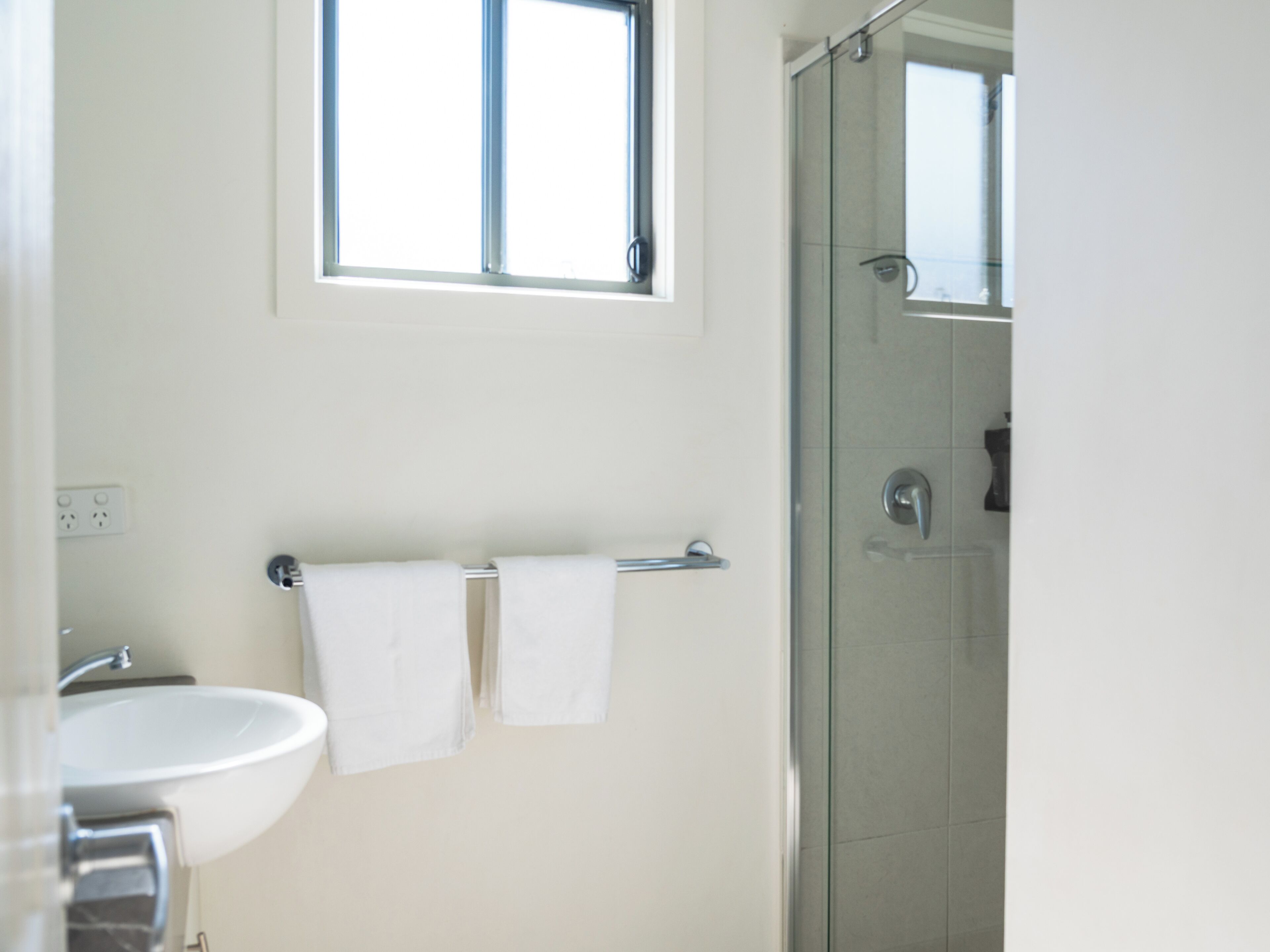 Un baño con lavamanos, cabina de ducha de vidrio y una ventana sobre el espejo.