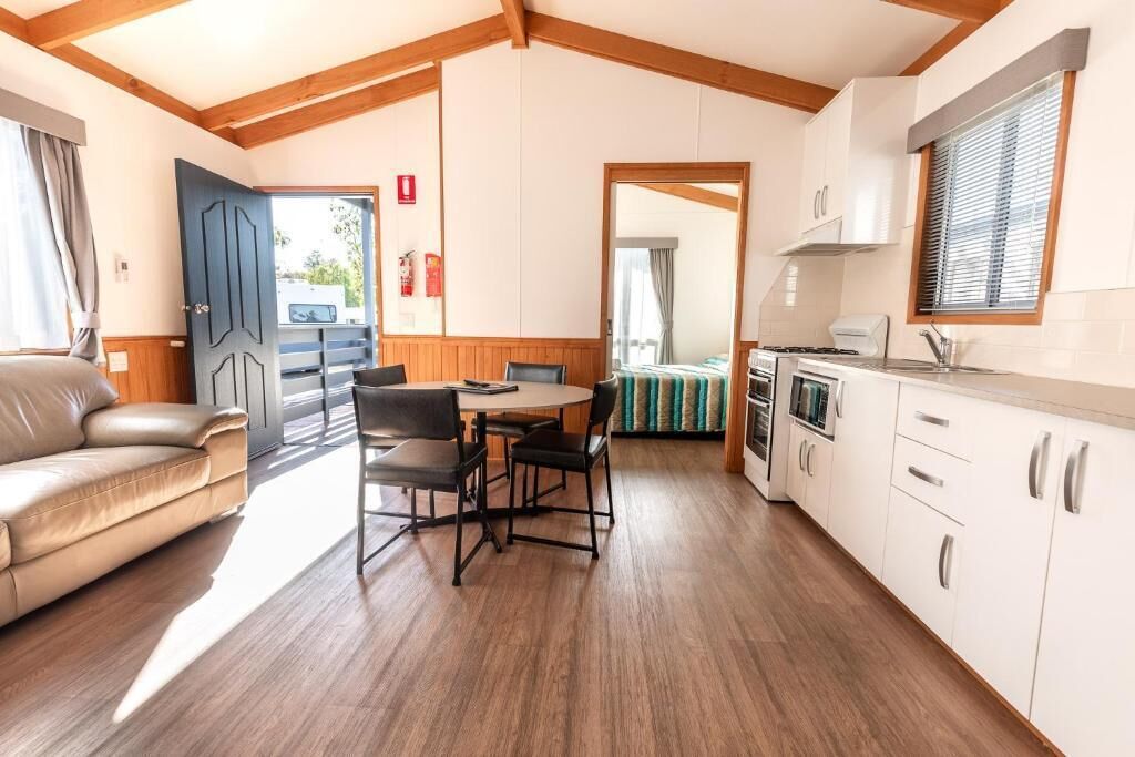 Ein gemütliches Zimmer mit Holzboden, einer Essecke mit Tisch und Stühlen, einer Küchenzeile mit Herd und einem Bett mit gestreifter Decke.