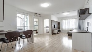 A spacious living area with a dining table, chairs, a TV, and a kitchenette. - B.Living (Curitiba)