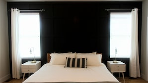 Un dormitorio con una cama, dos mesitas de noche y un ventanal con cortinas.