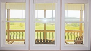 Vista a través de tres ventanas con barandillas de madera, cada una mostrando un paisaje verde y colinas.