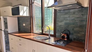 A modern kitchen with a wooden countertop, white cabinets, a stainless steel range hood, and a window with a view of greenery. - Blue Mountains studio, wild native garden full of birds, week-long stay 30% off (Hazelbrook)