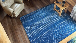 Interior acolhedor de uma cabana com um sofá de couro, uma televisão, um pequeno armário de madeira e um tapete azul estampado.