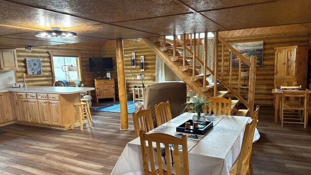 Interior de cabana de madeira com sala de jantar, cozinha e escada.