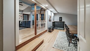Ett rymligt vardagsrum med en trätrappa som leder upp till ett loft, en matplats med ett långt bord och stolar samt ett kök i bakgrunden.