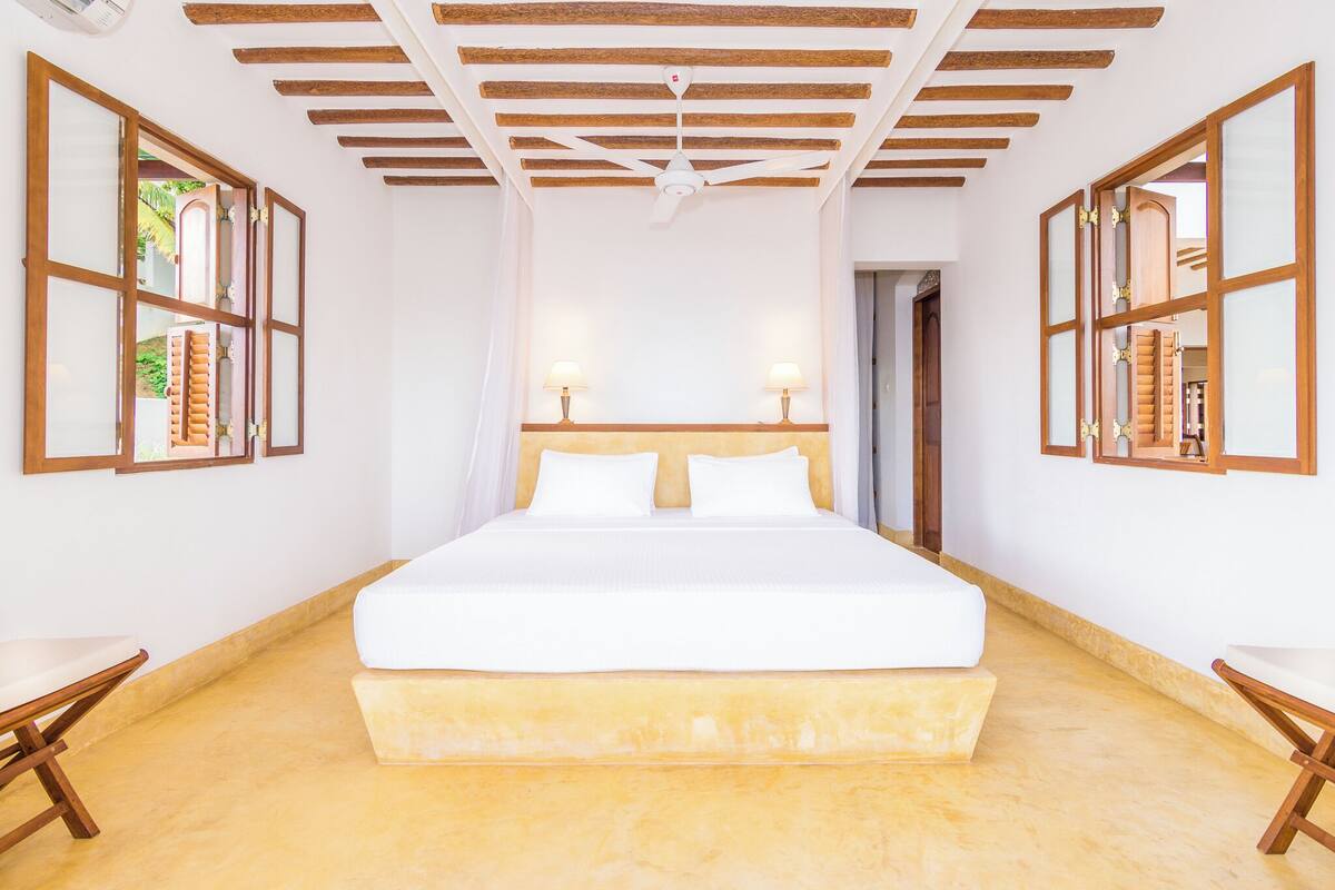 Un dormitorio amplio con una cama grande, vigas de madera en el techo y dos lámparas de noche.
