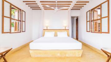 A spacious bedroom with a large bed, wooden ceiling beams, and two bedside lamps.