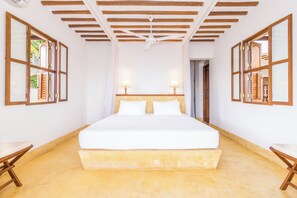 A spacious bedroom with a large bed, wooden ceiling beams, and two bedside lamps.