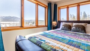 Un dormitorio con una cama grande, vistas a montañas y un lago, y una ventana con cortinas.