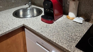 Cozinha com bancadas de granito, pia de aço inoxidável, cafeteira vermelha e armários de madeira.