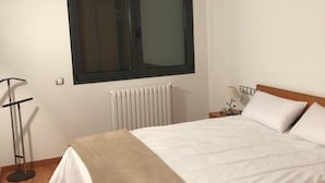 Quarto com cama, janela, radiador, mesa de cabeceira com luminária e um abajur.