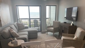 A living room with a sofa, two armchairs, a coffee table, and a TV mounted on the wall. - Shore Beats Work! Direct Oceanfront Atlantic Beach Paradise (Atlantic Beach)