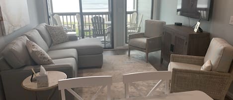 Una sala de estar con un sofá, dos sillones, una mesa de centro y un televisor montado en la pared.