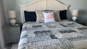 A neatly made bed with a patterned quilt, two bedside lamps, and a small bedside table with a lamp. - Shore Beats Work! Direct Oceanfront Atlantic Beach Paradise (Atlantic Beach)