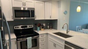 A modern kitchen with stainless steel appliances, white cabinetry, and a blue accent wall. - Shore Beats Work! Direct Oceanfront Atlantic Beach Paradise (Atlantic Beach)
