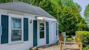 A white building with green shutters, a porch with a table and chairs, and a 'Welcome' sign.