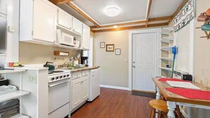 A compact kitchen with white cabinets, a stove, and a wooden dining table with stools.