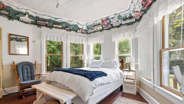 A bedroom with a bed, a chair, a bench, and large windows.