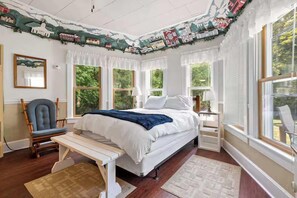 A bedroom with a bed, a chair, a bench, and large windows. - Charming Studio in Door County – Private: Ephraim (Ephraim)