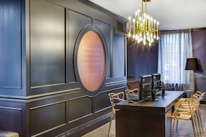 Een moderne hotellobby met een wand van donker hout, een ronde spiegel met een citaat, een kroonluchter, een receptiebalie en een zithoek met stoelen.