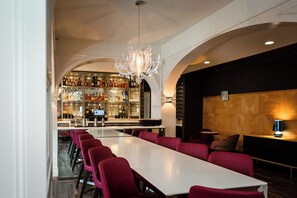 Een bar met een lange tafel en rode stoelen, een kroonluchter en een bar gevuld met flessen.