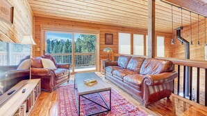 Ein großzügiges Wohnzimmer mit Holzbalkendecke und großen Fenstern, einer Ledersofa, einem Couchtisch und einem Bücherregal.
