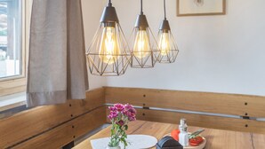 Ein Essbereich mit einer hölzernen Bank, einem Tisch mit Blumenvase und Pendelleuchten.