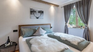 Ein Schlafzimmer mit einem Holz-Kopfteil, einem Bett mit weißer und grüner Bettwäsche, einem Bild von einem Reh und einem Fenster mit Vorhängen.