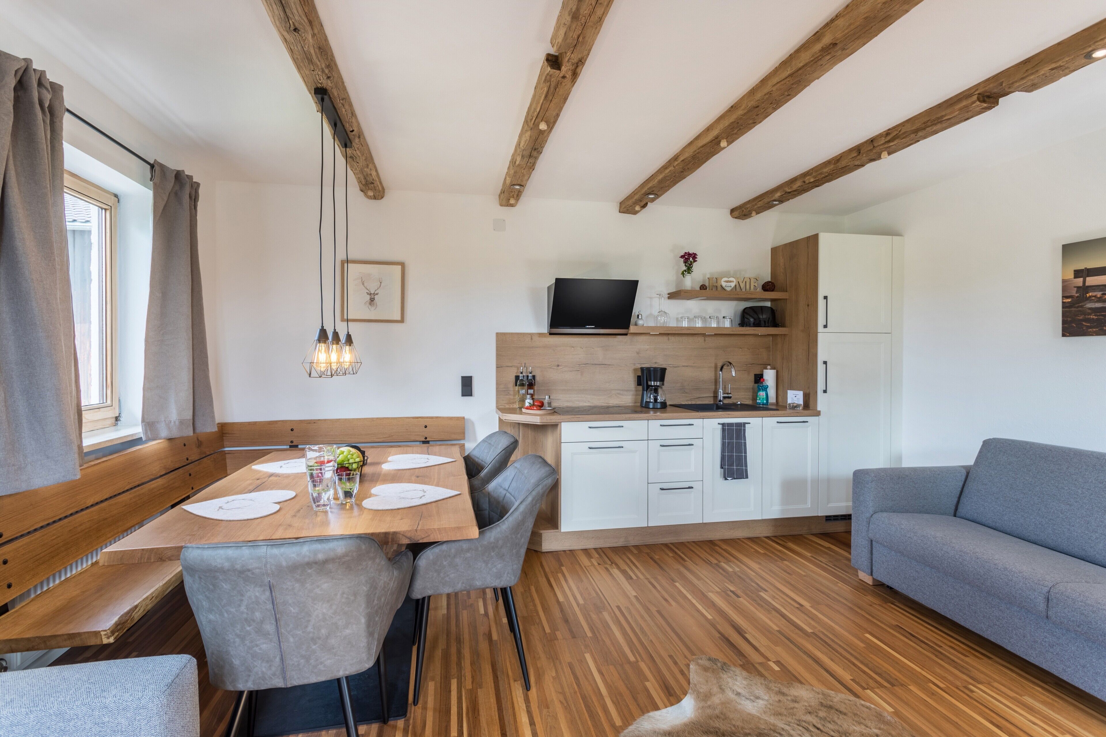 Una cucina moderna con travi in legno, un'area pranzo con tavolo e sedie in legno, e un divano grigio.