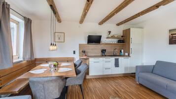 Una cucina moderna con travi in legno, un'area pranzo con tavolo e sedie in legno, e un divano grigio.